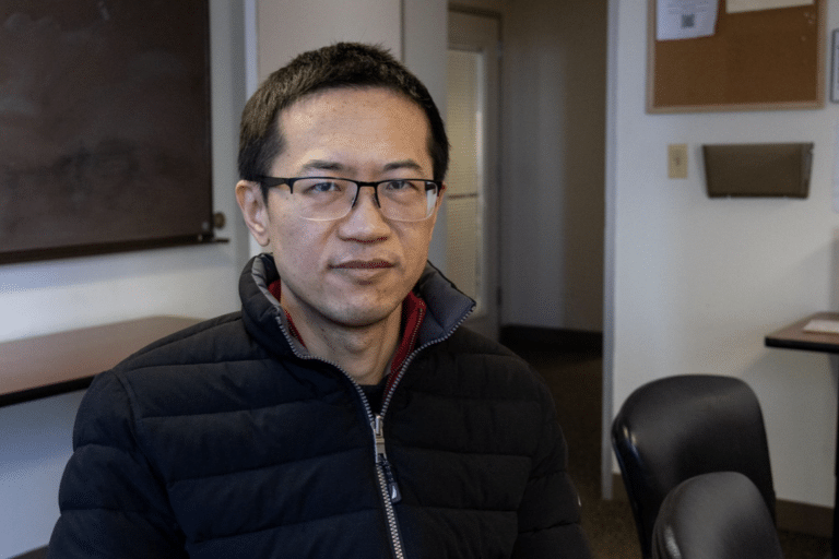Changwu Wang, a second-year student at the Pacific College of Health and Science, sits at a table in a classroom.